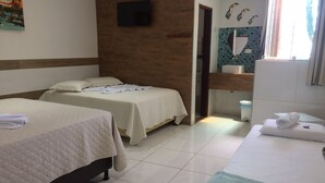 Quarto de hotel com duas camas, banheiro com parede azulejada e televisão de tela plana fixada na parede.