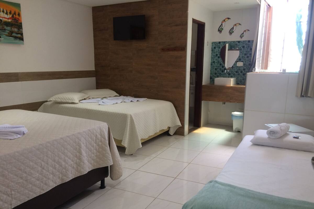 Une chambre d’hôtel avec deux lits, une salle de bain avec un mur carrelé et un téléviseur à écran plat fixé au mur.