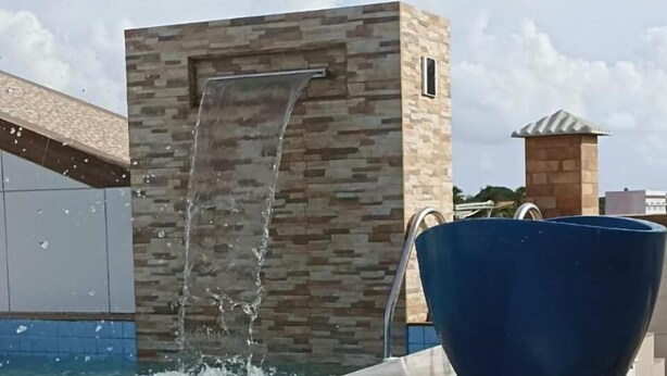 Piscina com cachoeira e uma grande bacia azul na borda.