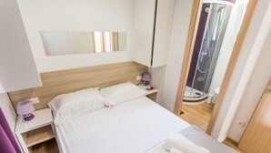 A hotel room with a bed, a nightstand, a lamp, a mirror, and a shower area.