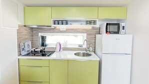 A compact kitchen with green cabinets, a white countertop, a stainless steel sink, a microwave, and a refrigerator.