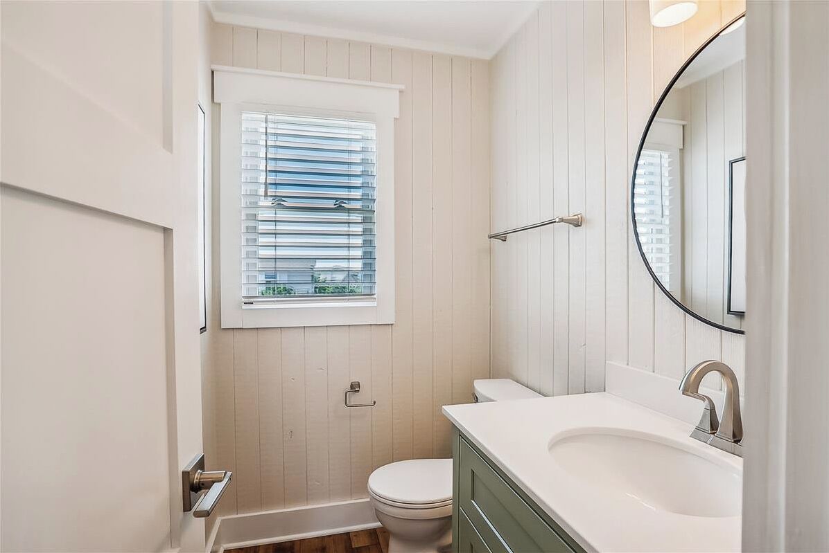 Une salle de bain avec des toilettes blanches, un lavabo doté d’un robinet moderne et une fenêtre avec des stores.