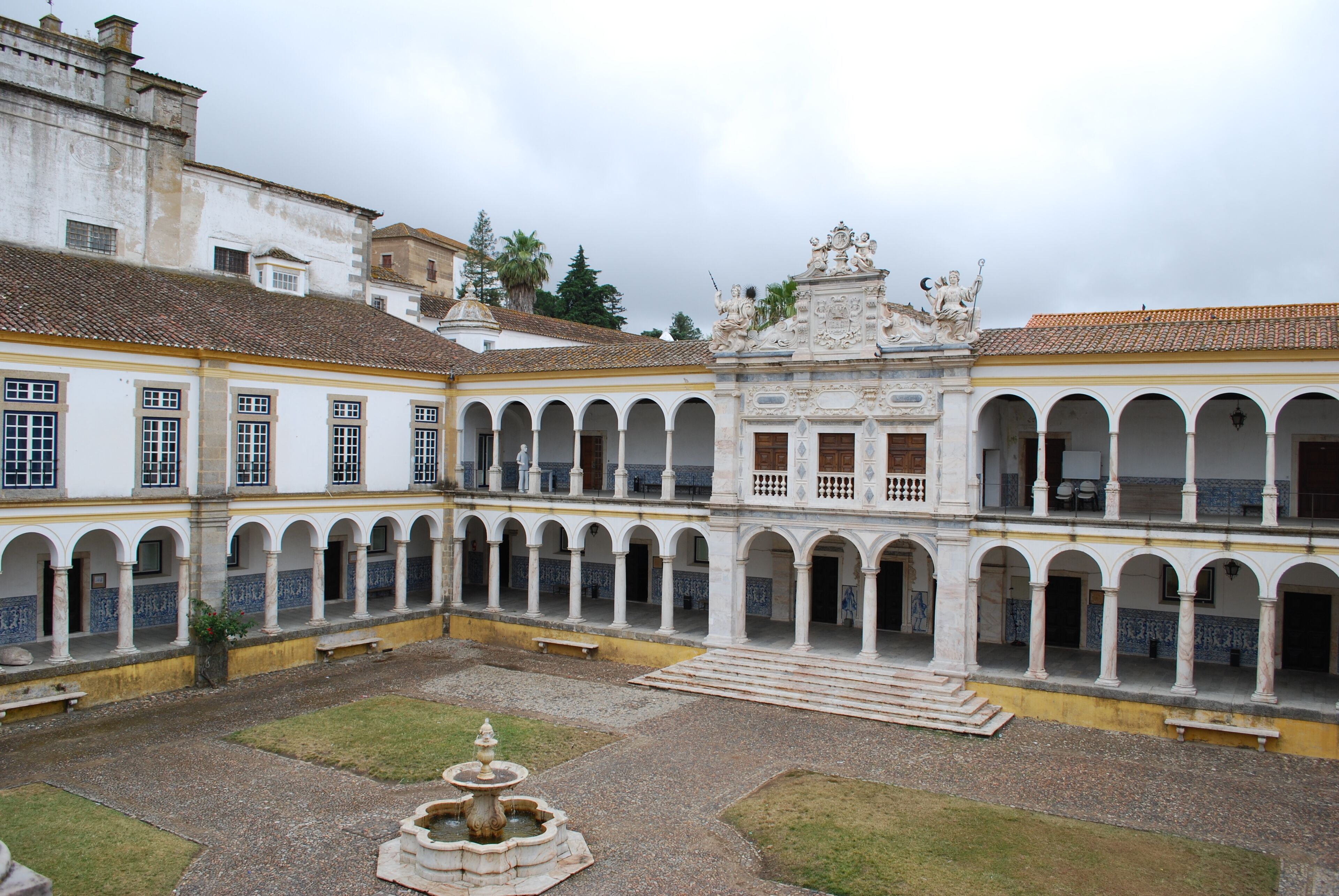 A courtyard with a fountain, surrounded by white buildings with multiple arches and balconies.