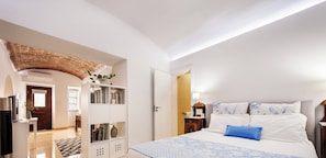 Habitación de hotel moderna con una cama grande, un armario, un escritorio y un baño visible a través de una puerta abierta.