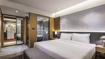 A modern hotel room with a large bed, a walk-in closet, a bathroom with a shower, and a wall-mounted map.