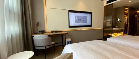 A hotel room with a bed, a desk, a chair, a television, and a minibar.
