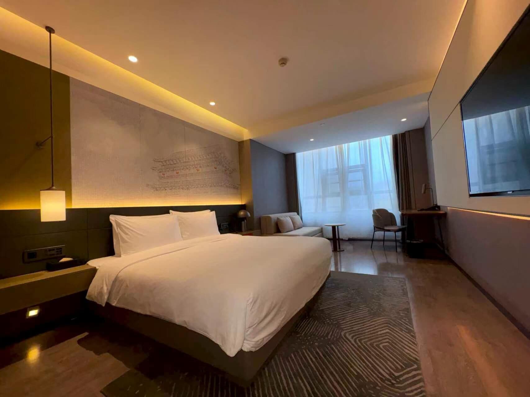 Una habitación de hotel moderna con una cama grande, un área de descanso, un escritorio y un ventanal amplio.