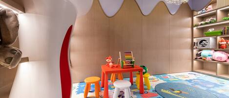 A children's playroom with a colorful play mat, a small table with toys, and a bookshelf with stuffed animals.