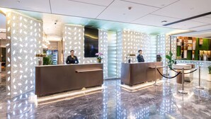 Un moderno vestíbulo de hotel con dos mostradores de recepción, suelo de mármol y paredes con diseño.