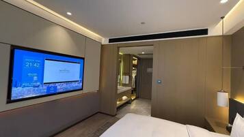 Ein modernes Hotelzimmer mit einem großen Flachbildfernseher an der Wand, einem Bett, einem Nachttisch und einem begehbaren Kleiderschrank.
