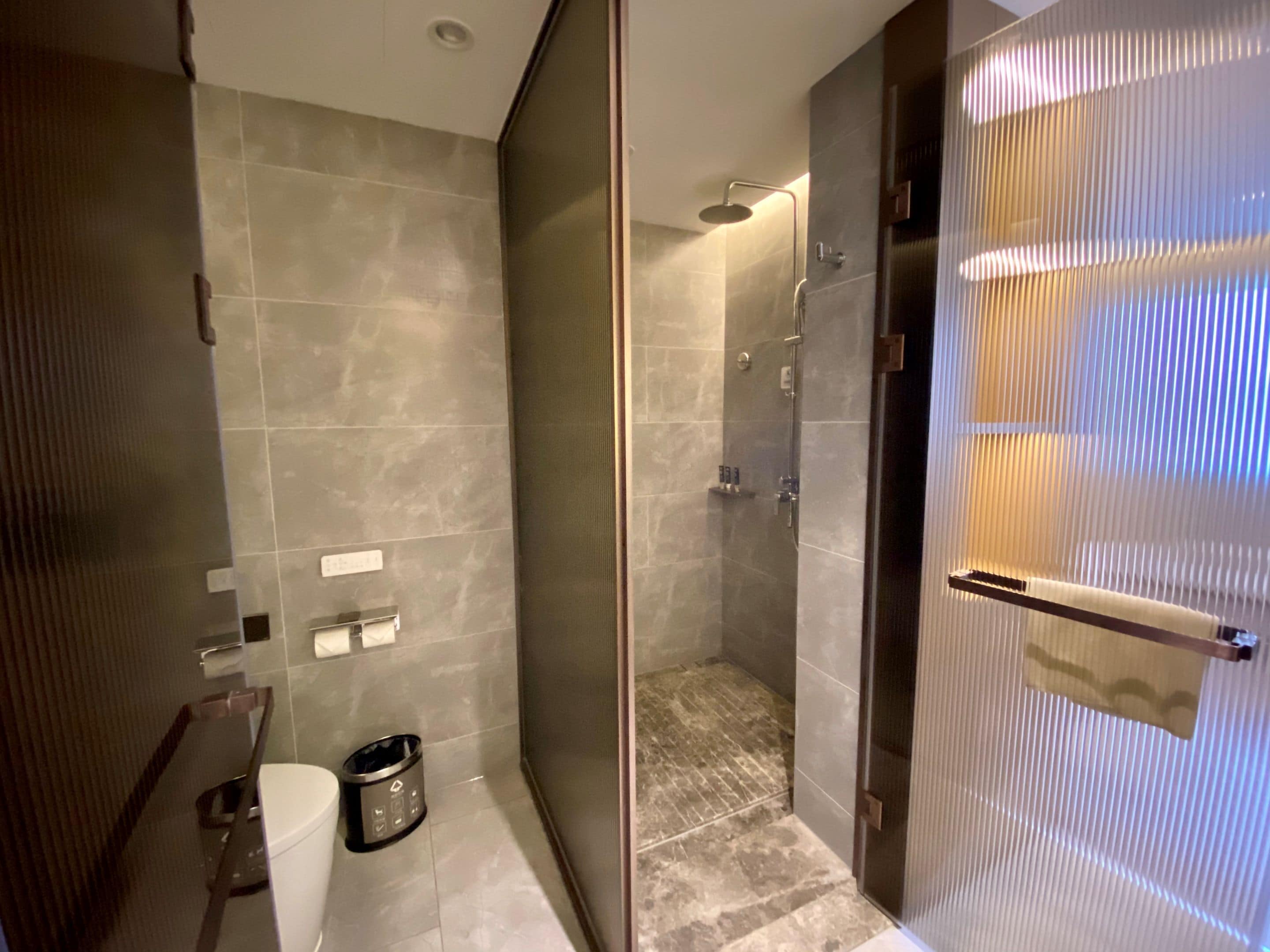 A modern bathroom with a glass-enclosed shower, a toilet, and a trash bin.