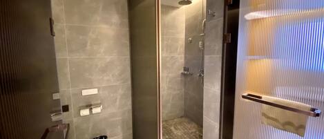A modern bathroom with a glass-enclosed shower, a toilet, and a trash bin.