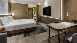 Una habitación de hotel moderna con una cama grande, un escritorio, un televisor de pantalla plana y un vestidor.