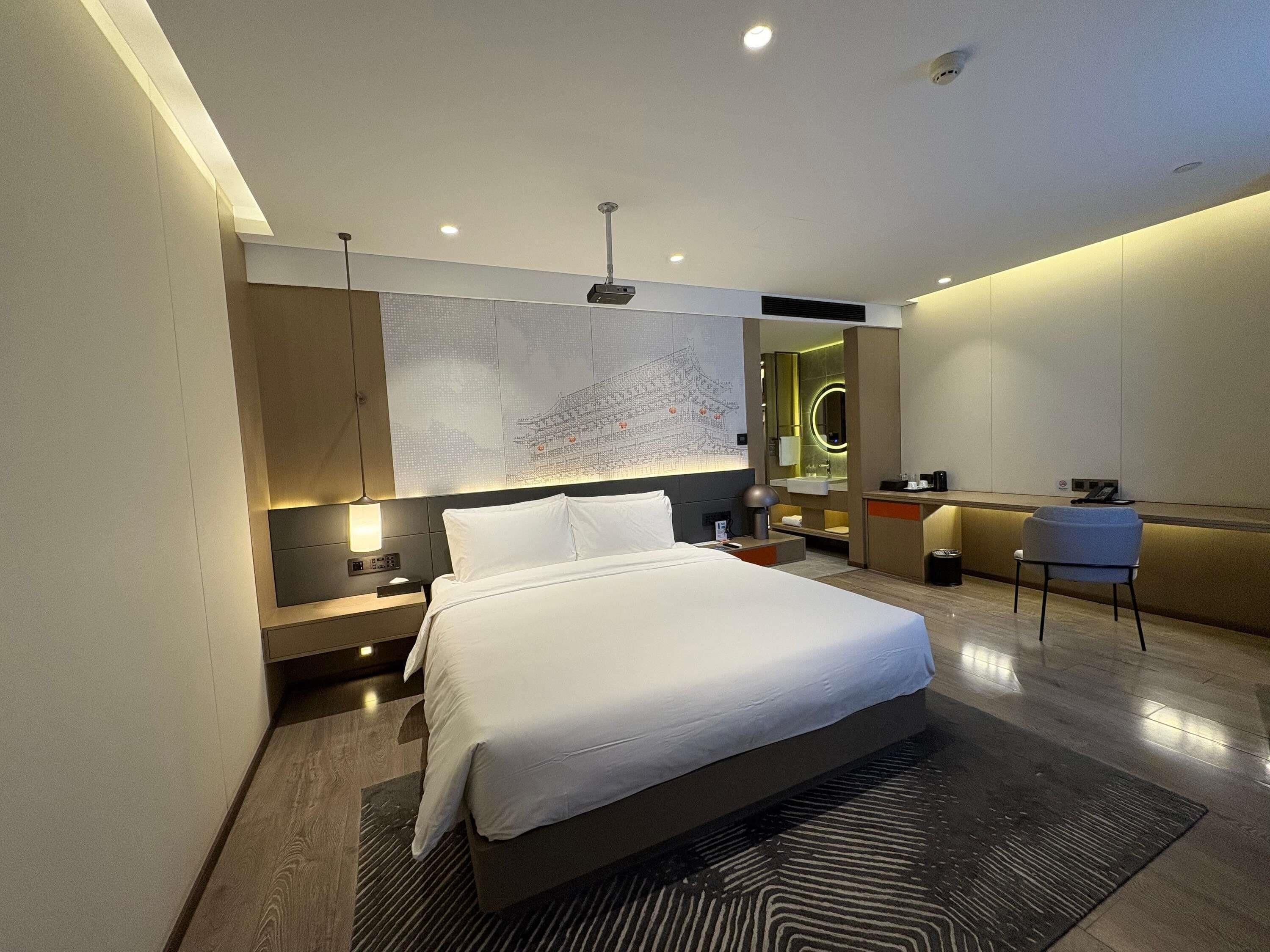 A modern hotel room with a large bed, a desk, a chair, a mirror, and a wall-mounted map.