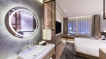 Una habitación de hotel moderna con una cama grande, un espejo redondo, una bañera y un televisor.