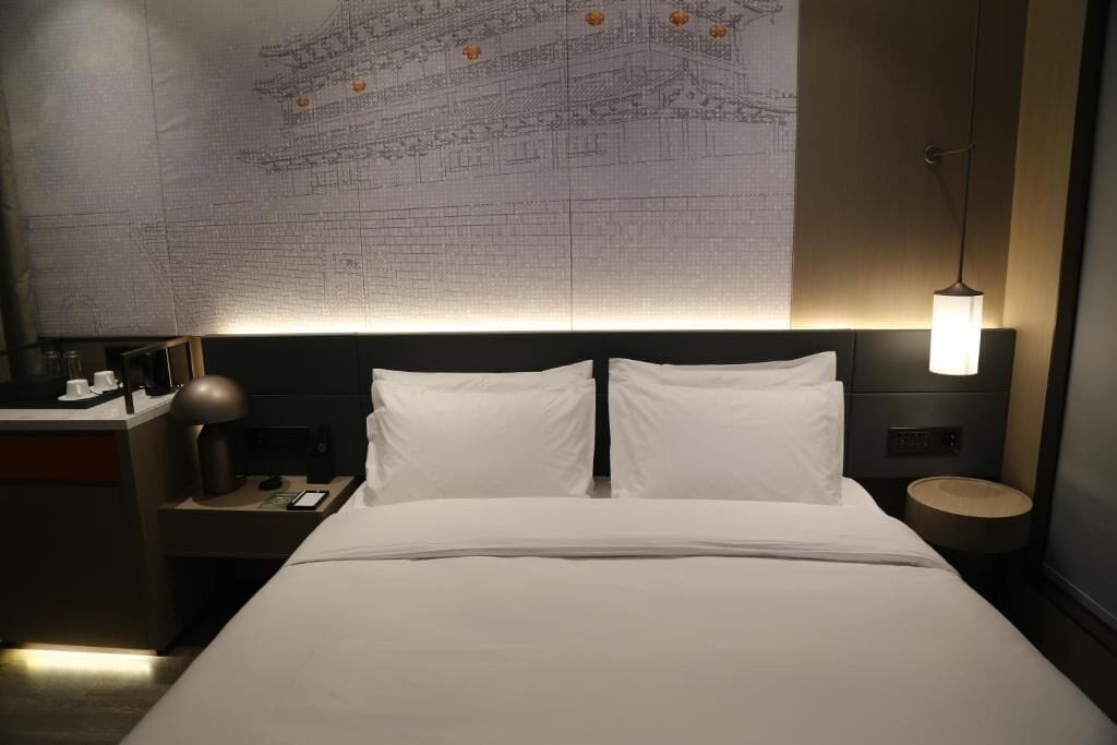 Ein Hotelzimmer mit einem Bett, einem Nachttisch, einer Lampe und einer Wand mit einer Karte.