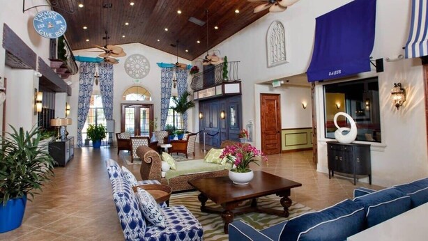 Eine geräumige Lobby mit hoher Decke, Holzbalken und verschiedenen Sitzbereichen, darunter Sofas und ein Esstisch.