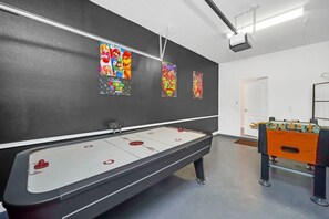A room with a foosball table, a shuffleboard table, and wall art featuring video game characters.