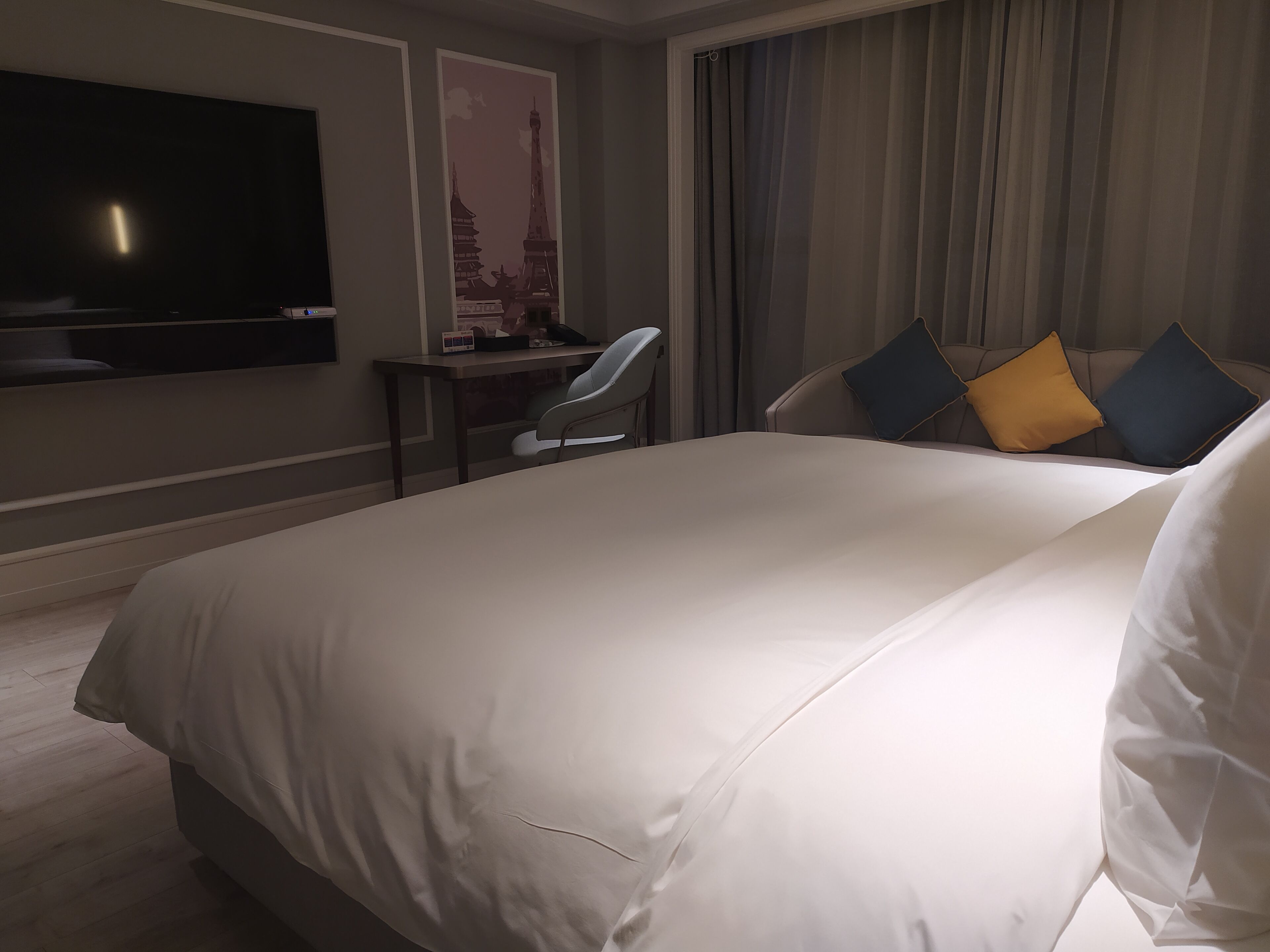 Habitación de hotel con una cama grande, un escritorio, una silla, un televisor y vistas a la ciudad.