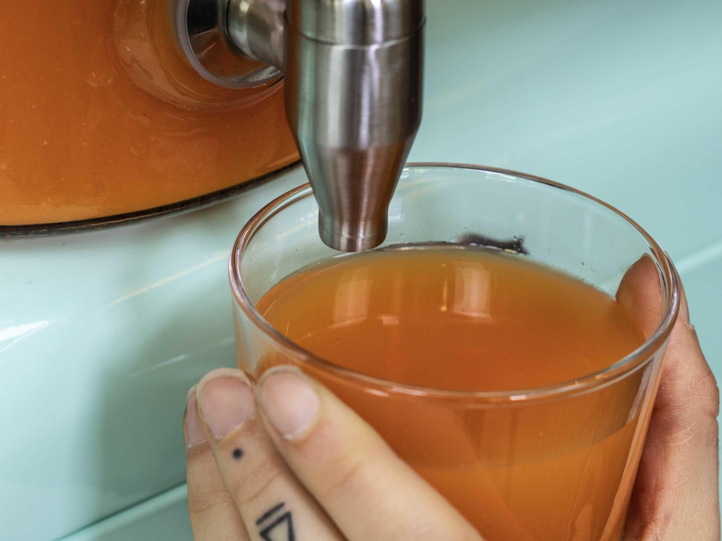 Una mano sosteniendo una taza de vidrio con un infusor metálico para té.