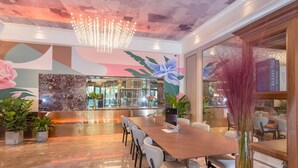 A modern dining area with a long wooden table, white cushioned chairs, and a decorative chandelier. - Mercure Hangzhou East Railway Station (Hangzhou)