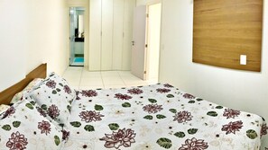 A bedroom with a bed covered in floral bedding, a wooden headboard, and a white door leading to another room.