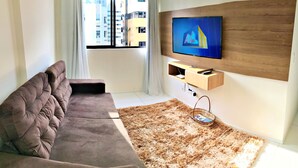 A modern living room with a sofa, a TV mounted on a wooden panel, and a window with curtains. - Vacanze - Golden Place 503 (Maceió)