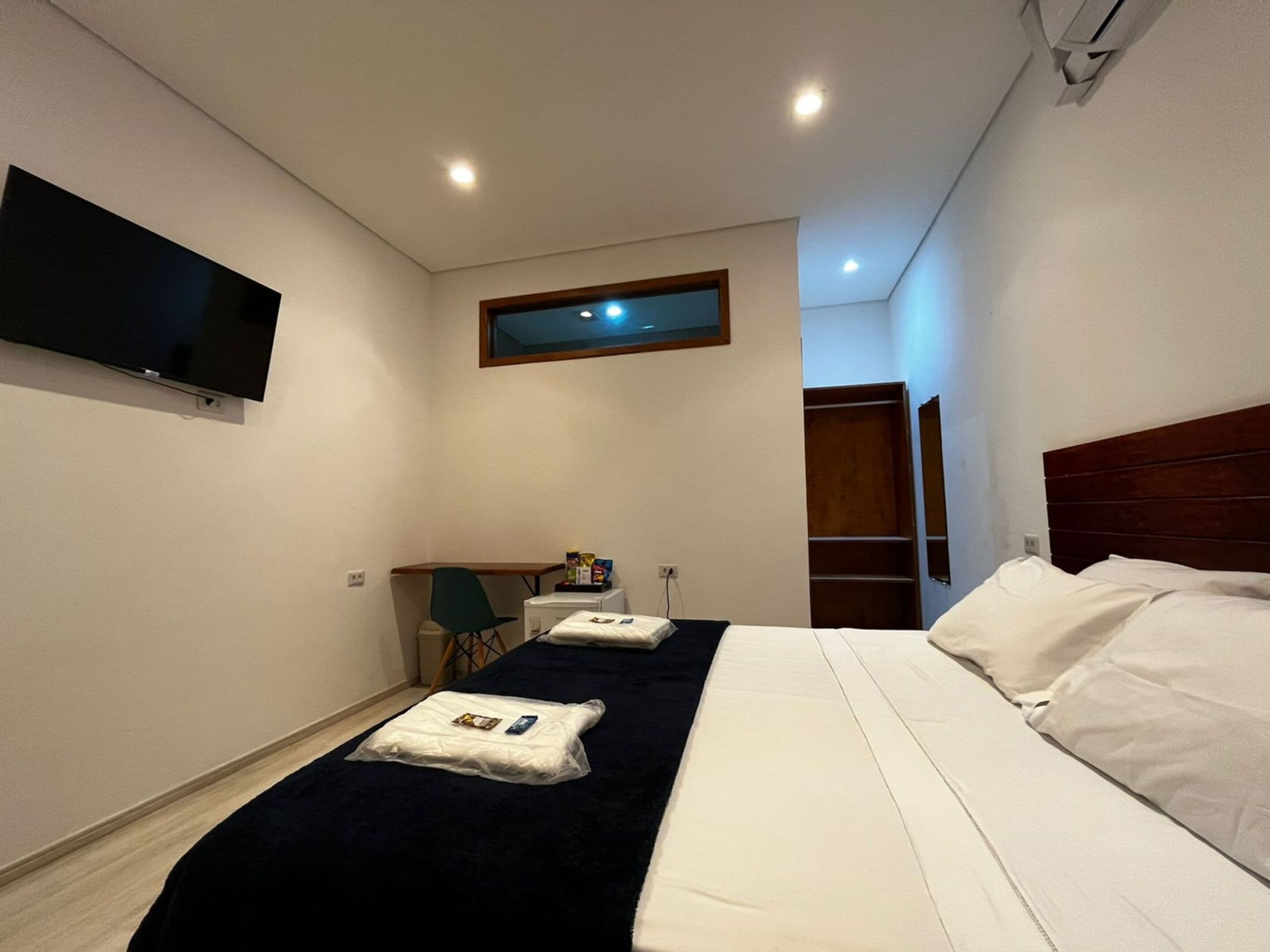 Ein Hotelzimmer mit Bett, Schreibtisch, Stuhl, Wandfernseher und Fenster.