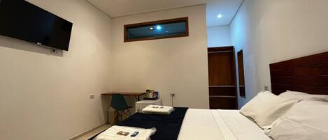 Ein Hotelzimmer mit Bett, Schreibtisch, Stuhl, Wandfernseher und Fenster.
