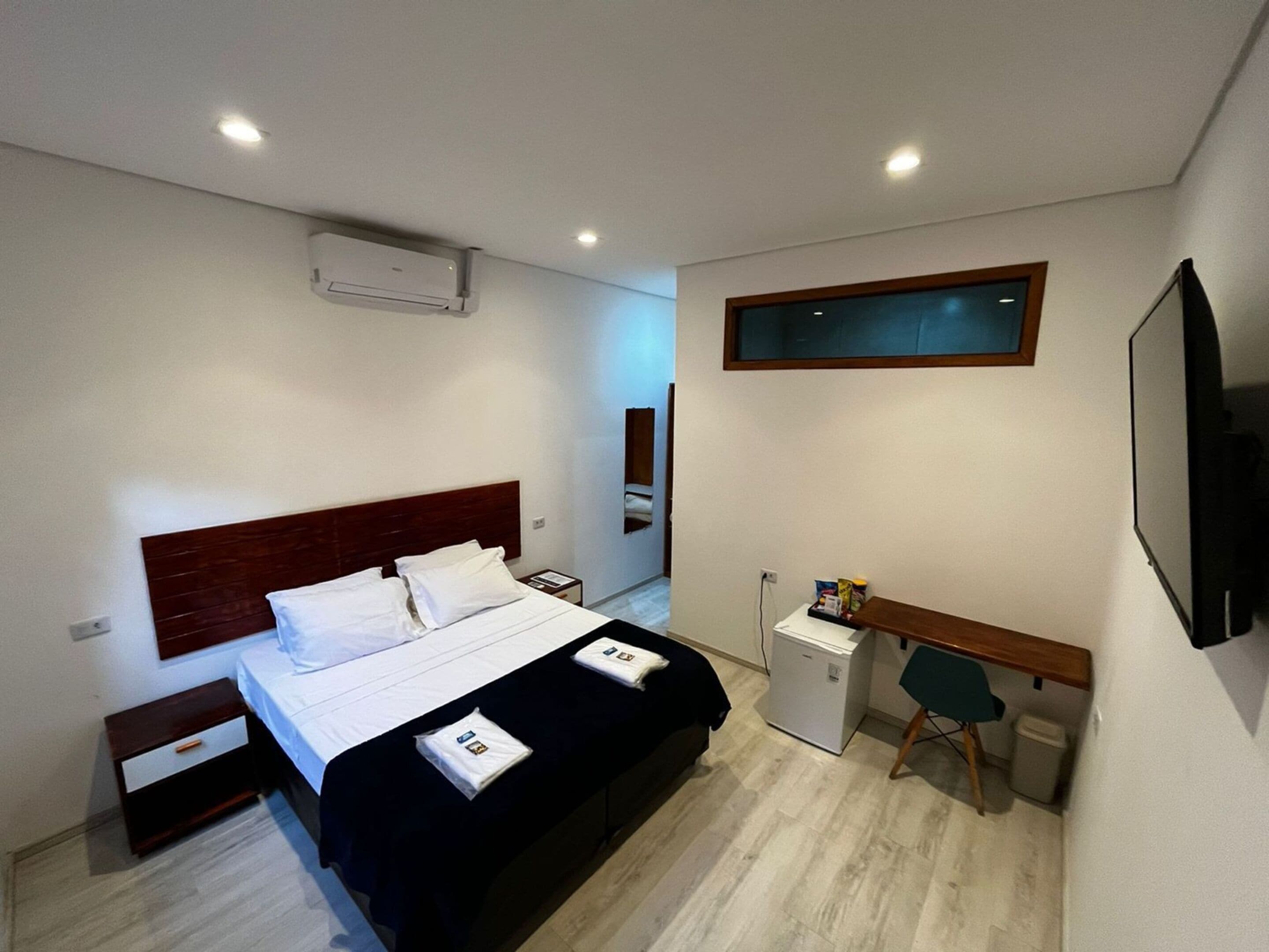 Een hotelkamer met een bed, nachtkastjes, een bureau, een stoel, een kleine koelkast en een aan de muur bevestigde televisie.