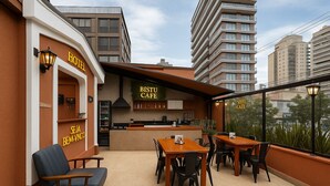 Een hotel met een BISTU CAFE, een buitenzitgedeelte met tafels en stoelen, en uitzicht op de skyline.