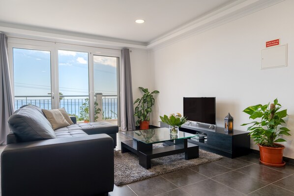 A modern living room with a sofa, a glass coffee table, a flat-screen TV, and potted plants.