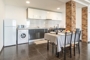 A modern kitchen with a dining area, featuring a washing machine, microwave, and a brick accent wall.