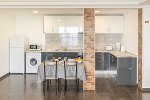 A compact kitchen with a dining area, including a washing machine, microwave, and a brick accent wall.