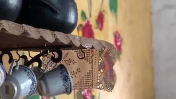 Primer plano de una maceta de cerámica negra sobre una estantería con encaje, sobre un fondo de papel tapiz floral.