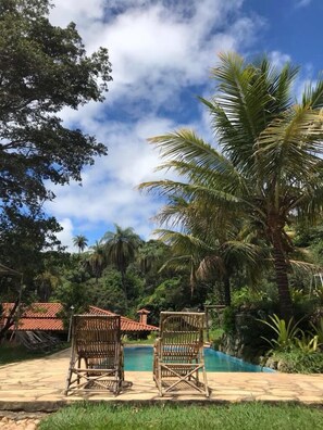 Uma área de piscina com duas cadeiras de vime, cercada por vegetação exuberante e palmeiras.