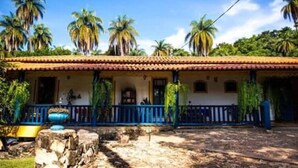 Un edificio de estilo colonial con techo de tejas, un porche con barandillas azules y palmeras al fondo.