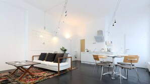 Un salon moderne avec un canapé blanc, une table à manger avec des chaises, et un coin cuisine à l’arrière-plan.
