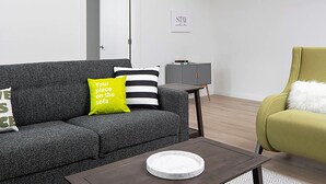A modern living room with a grey sofa, a green armchair, a small table, and a cabinet. - Stay Alfred at Riverfront Park (Spokane)