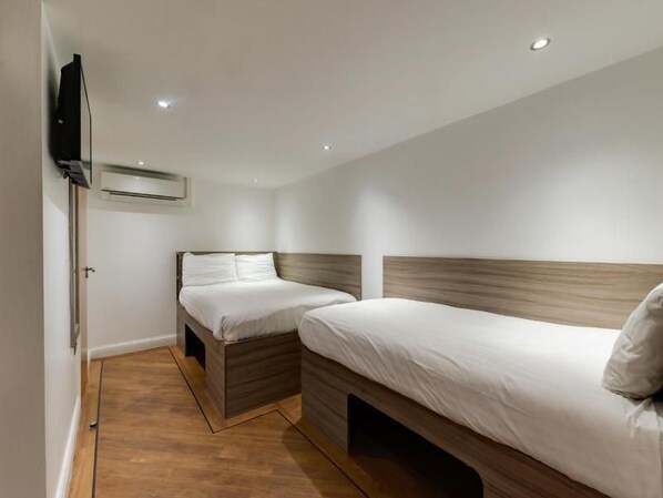 A hotel room with two beds, a flat-screen TV mounted on the wall, and an air conditioning unit.