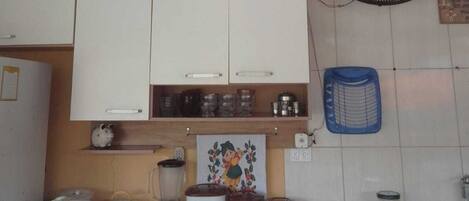 Una cuina amb armaris blancs, un mesclador, una cocedora d'arròs i un ventilador.