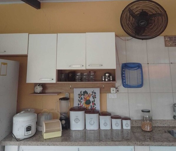 Una cocina con armarios blancos, una licuadora, una cocedora de arroz y un ventilador.