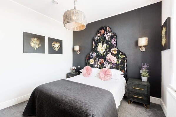 Une chambre à coucher comprenant un lit, une table de chevet, une lampe fixée au mur et une tête de lit décorative.