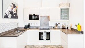 Eine moderne Küche mit weißen Schränken, einer Edelstahlspüle, einer Mikrowelle, einem Einbauofen und einem Toaster. An der Wand hängt ein Gemälde und auf der Arbeitsfläche steht ein Korb.