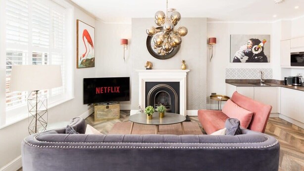 Ein Wohnzimmer mit Kamin, einem Fernseher, der 'NETFLIX' anzeigt, und einer modernen Deckenleuchte.