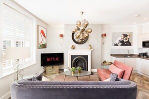 Un salon doté d’une cheminée, d’un téléviseur diffusant du contenu « NETFLIX », et d’un lustre moderne.