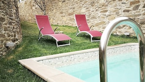 A swimming pool with two red lounge chairs and a stone wall in the background. - Holiday Villa in Douro Valley - Unesco Heritage (Peso da Régua)