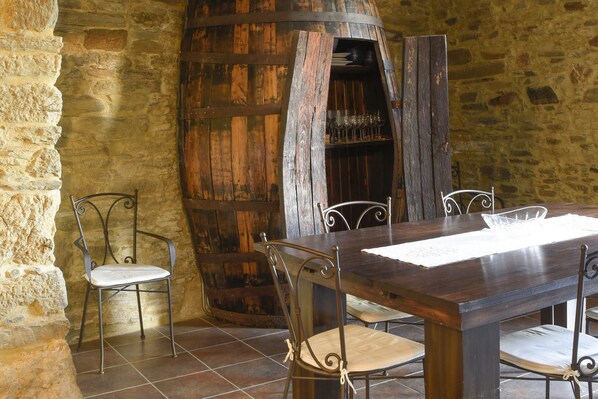 Un coin repas rustique avec une table en bois et des chaises en métal, un mur en pierre et un tonneau.
