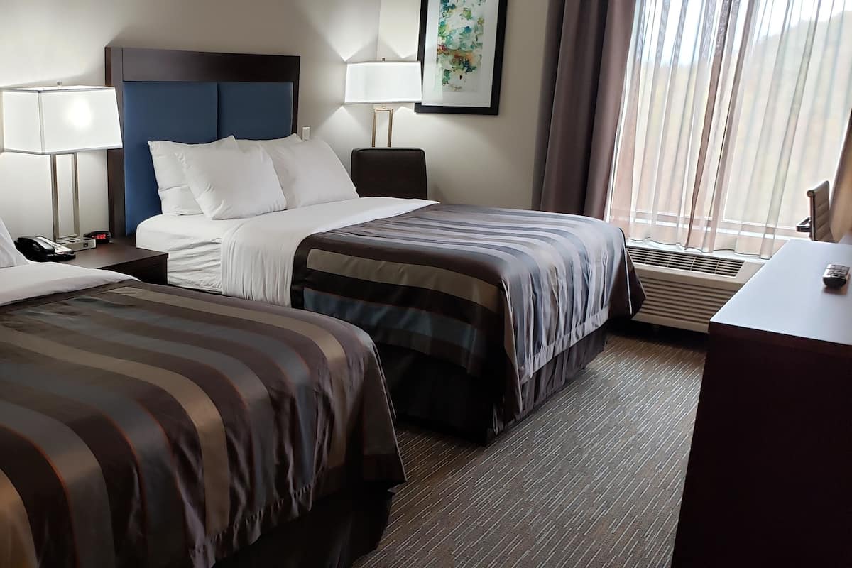 Une chambre d’hôtel avec deux lits, un bureau, une chaise, un téléphone et une fenêtre avec des rideaux.