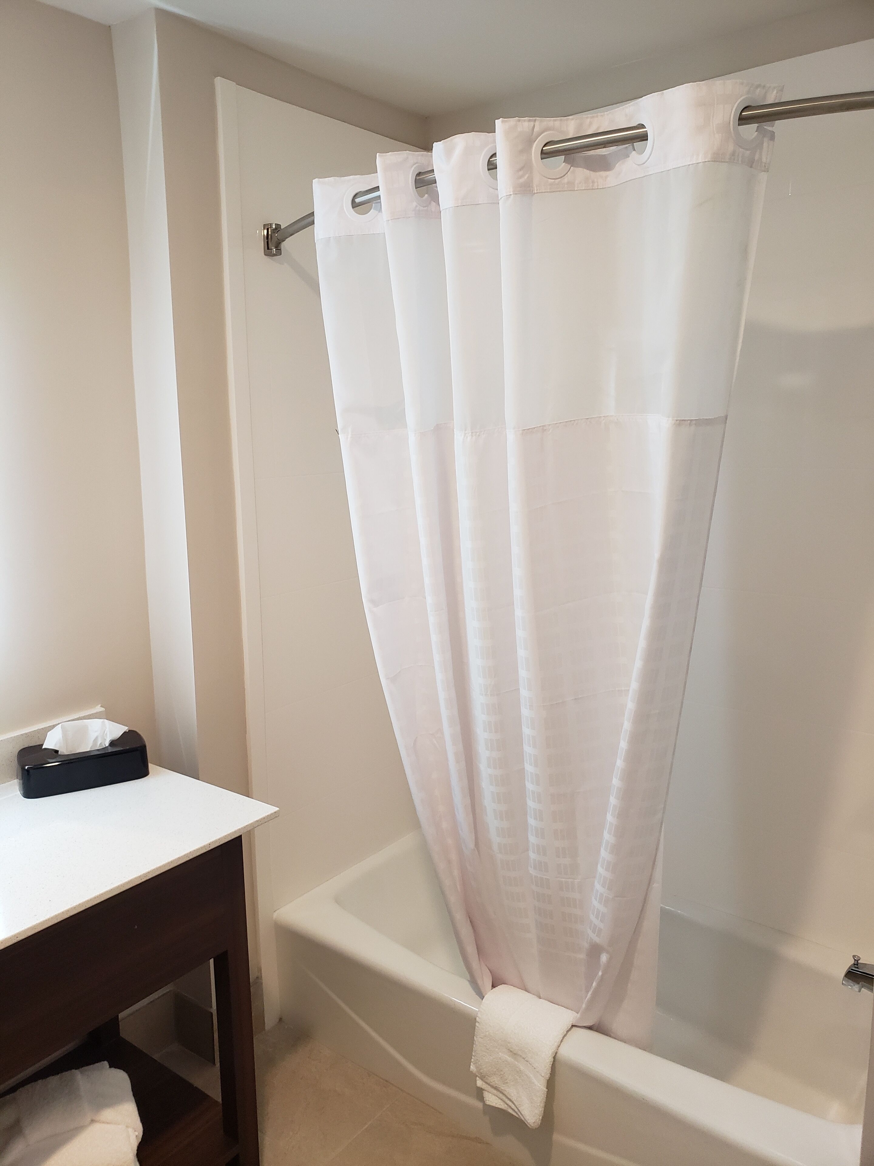 A bathroom with a bathtub, a white towel, and a black tissue box on a wooden table.